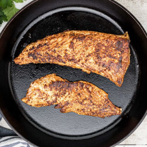 Overhead shot of two pieces of blackened redfish in a cast iron skillet.