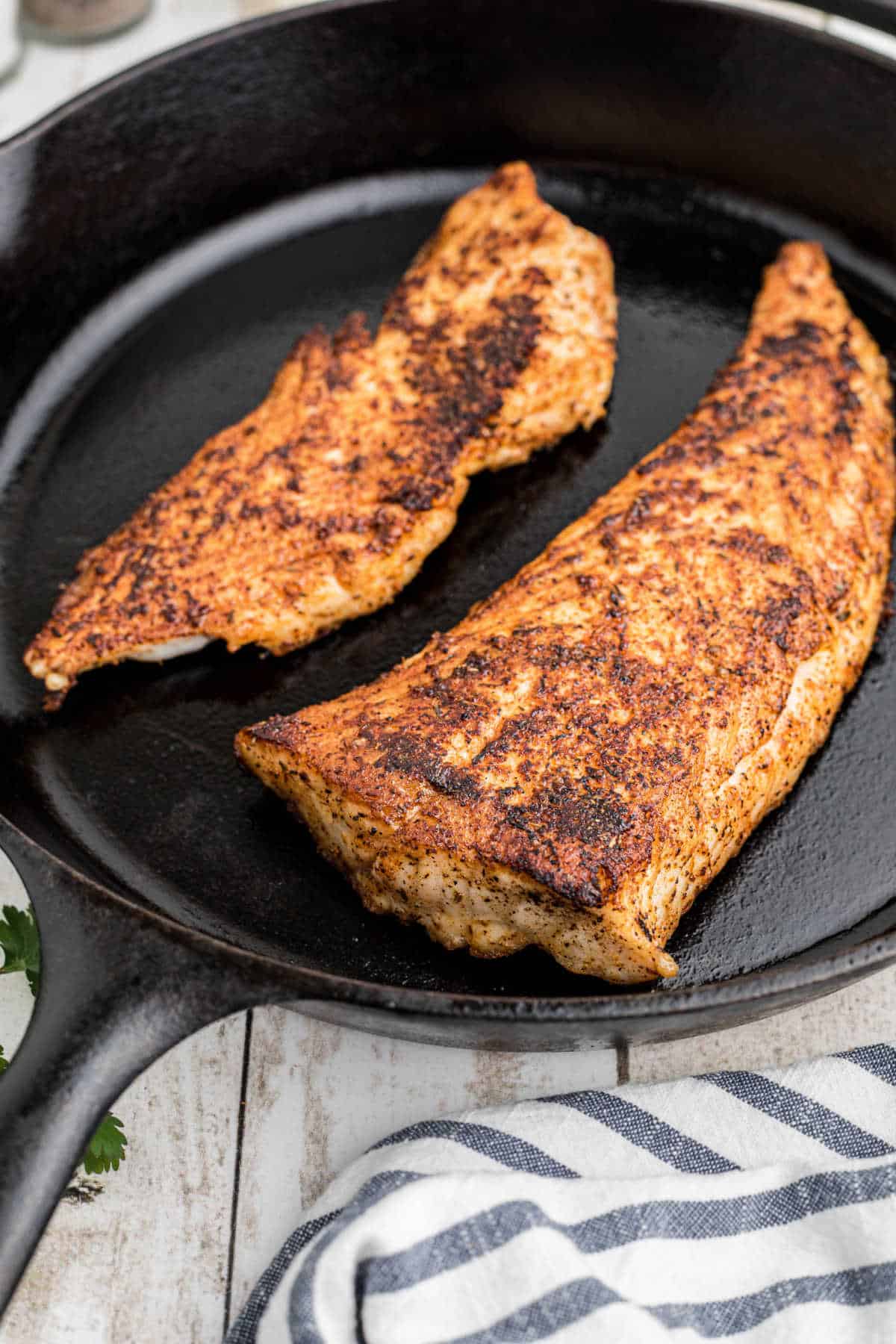 Two pieces of blackened redfish in a skillet from the side.