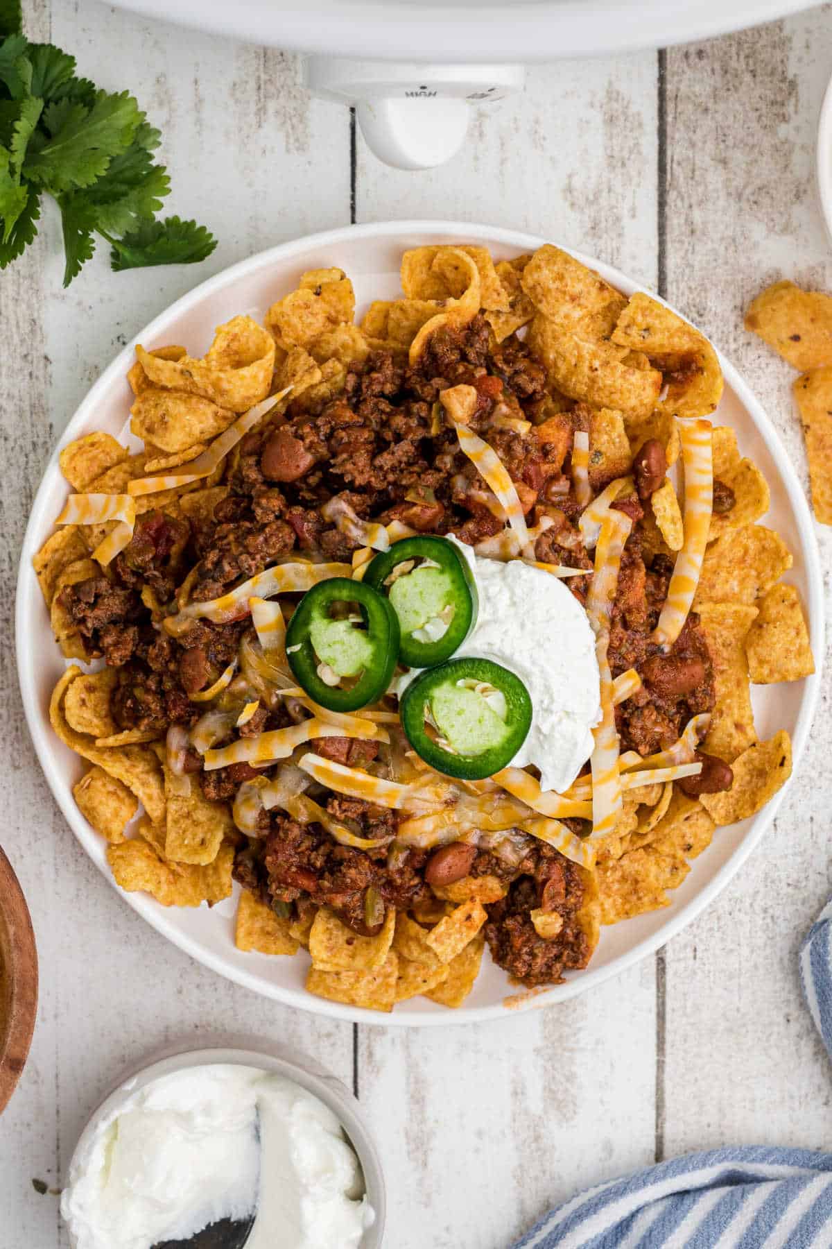 An overhead shot of a plate of crockpot frito pie with some sour cream and cheese.