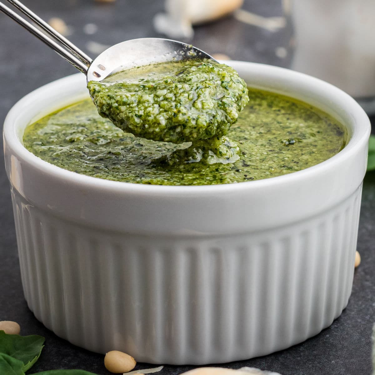 Close up of a bowl of pesto dressing with a spoon digging in.