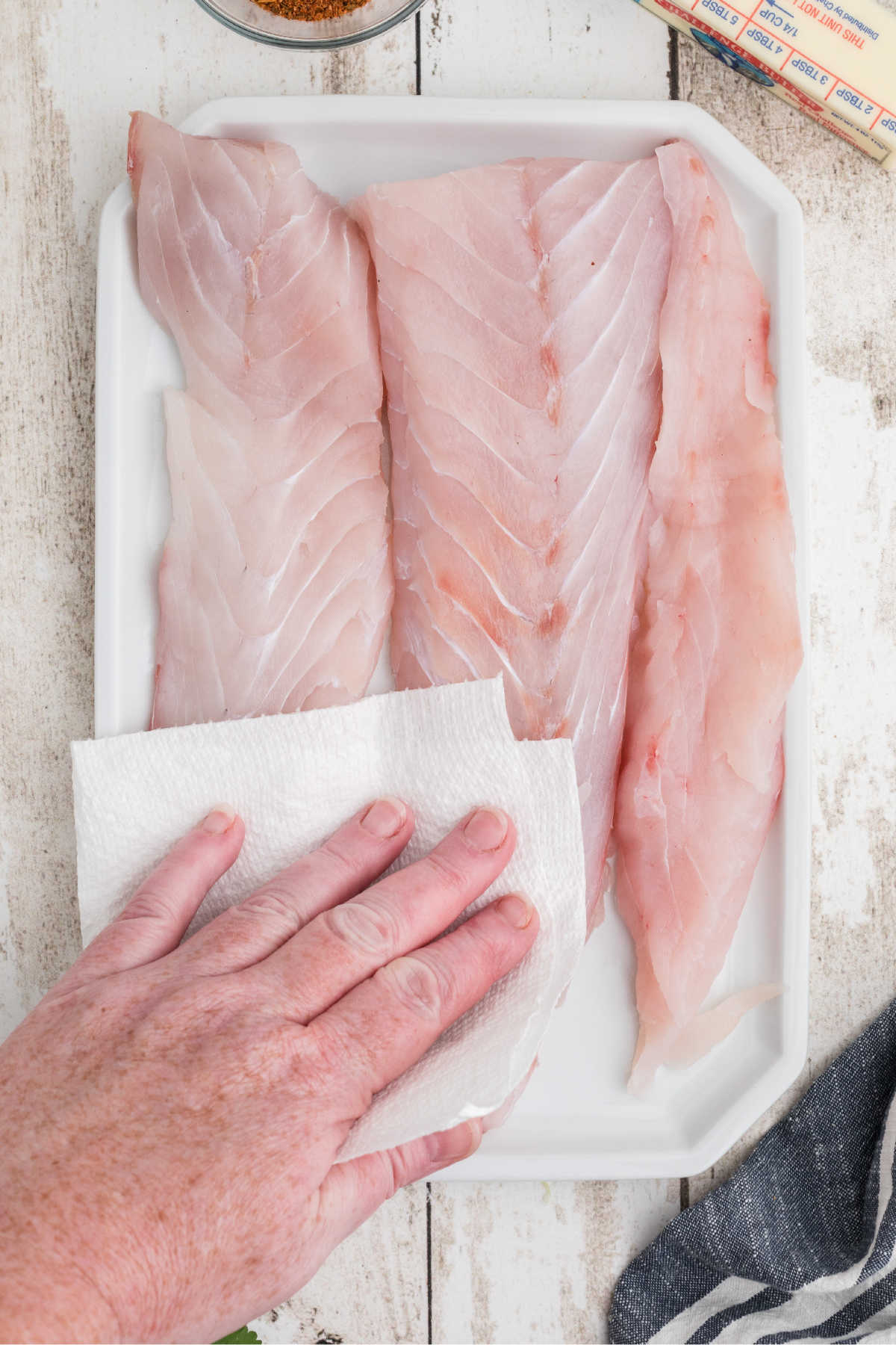 A plate full of redfish fillets, being patted dry with some paper towel.