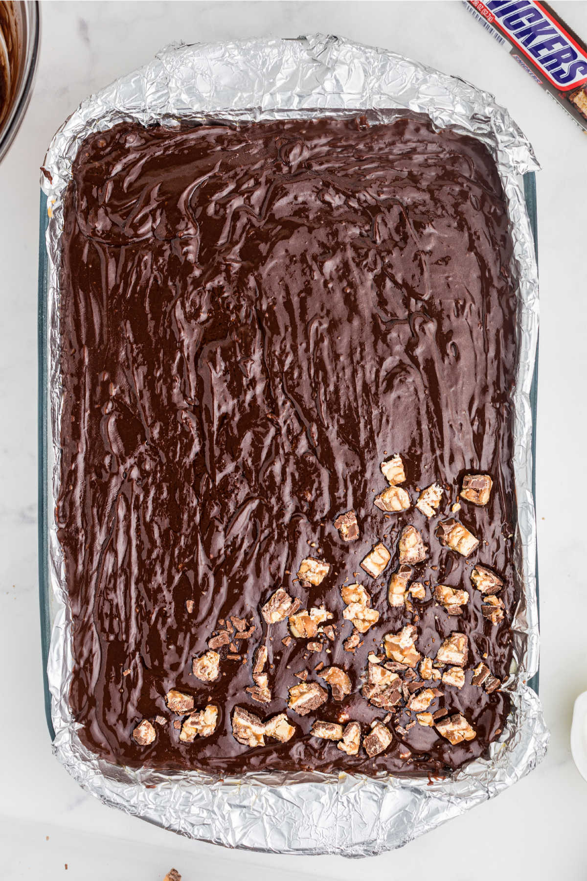 Chocolate poured on top of a nougat layer, with chopped snickers being sprinkled on top.