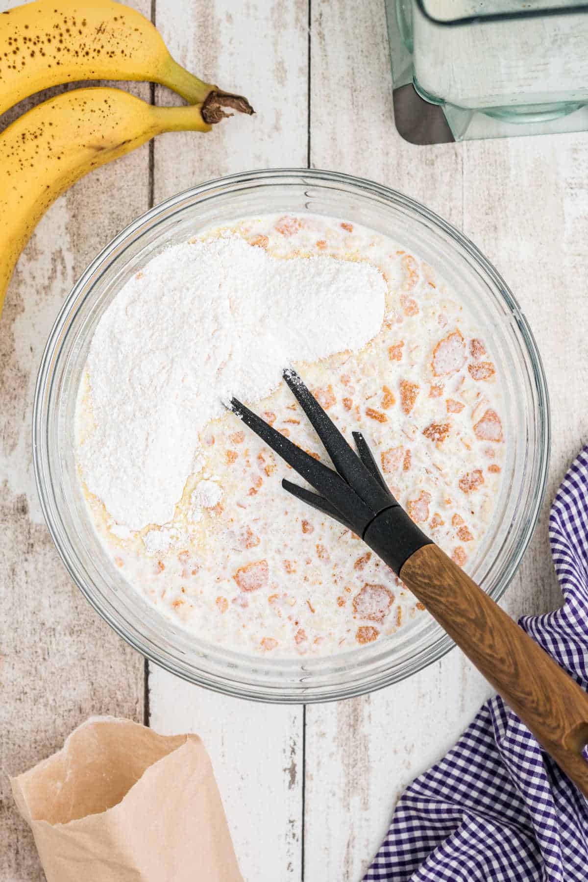 Pudding mix being added to a mixing bowl with cookies, bananas and cream.