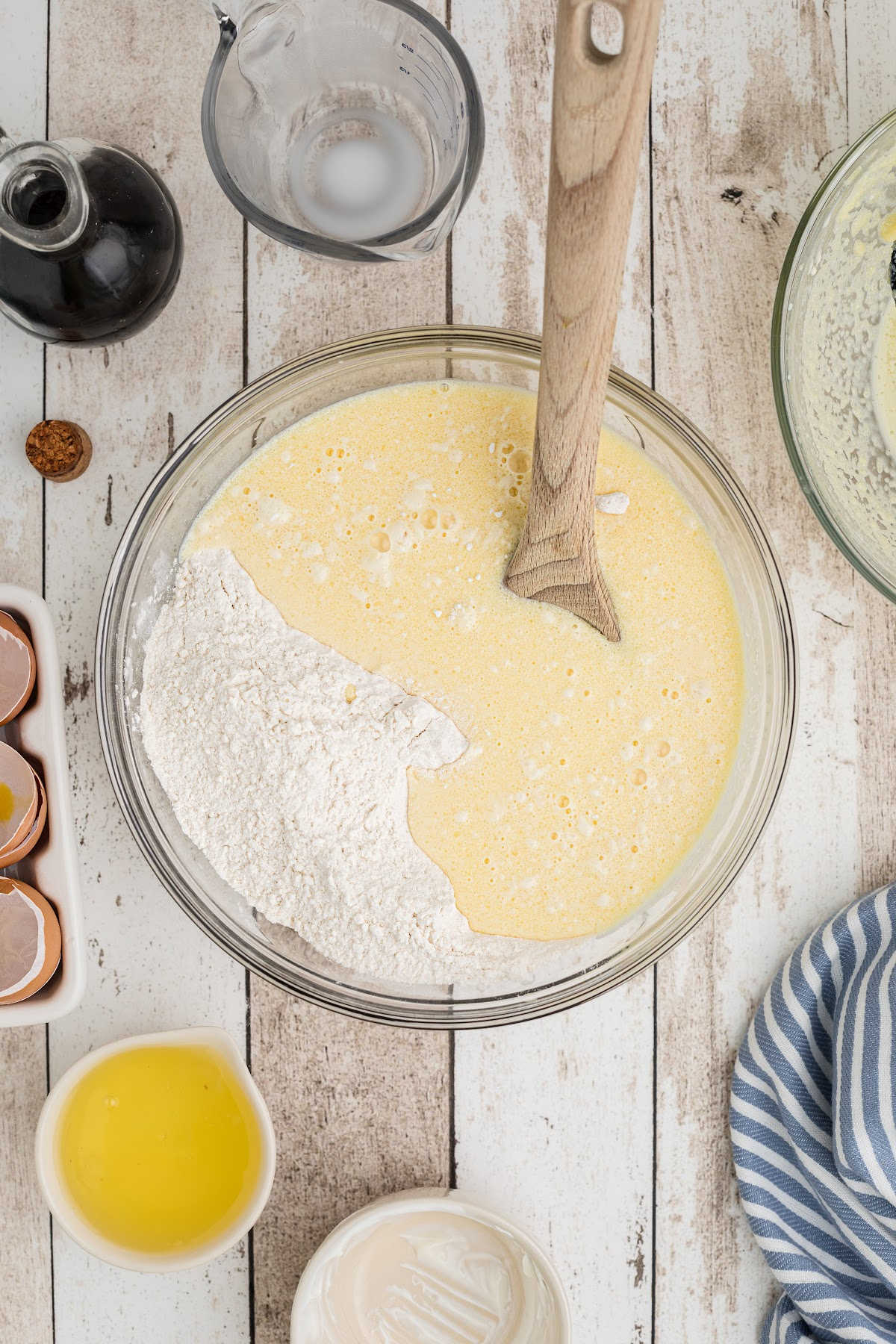 A large mixing bowl with a egg mixture being mixed with a flour mixture.