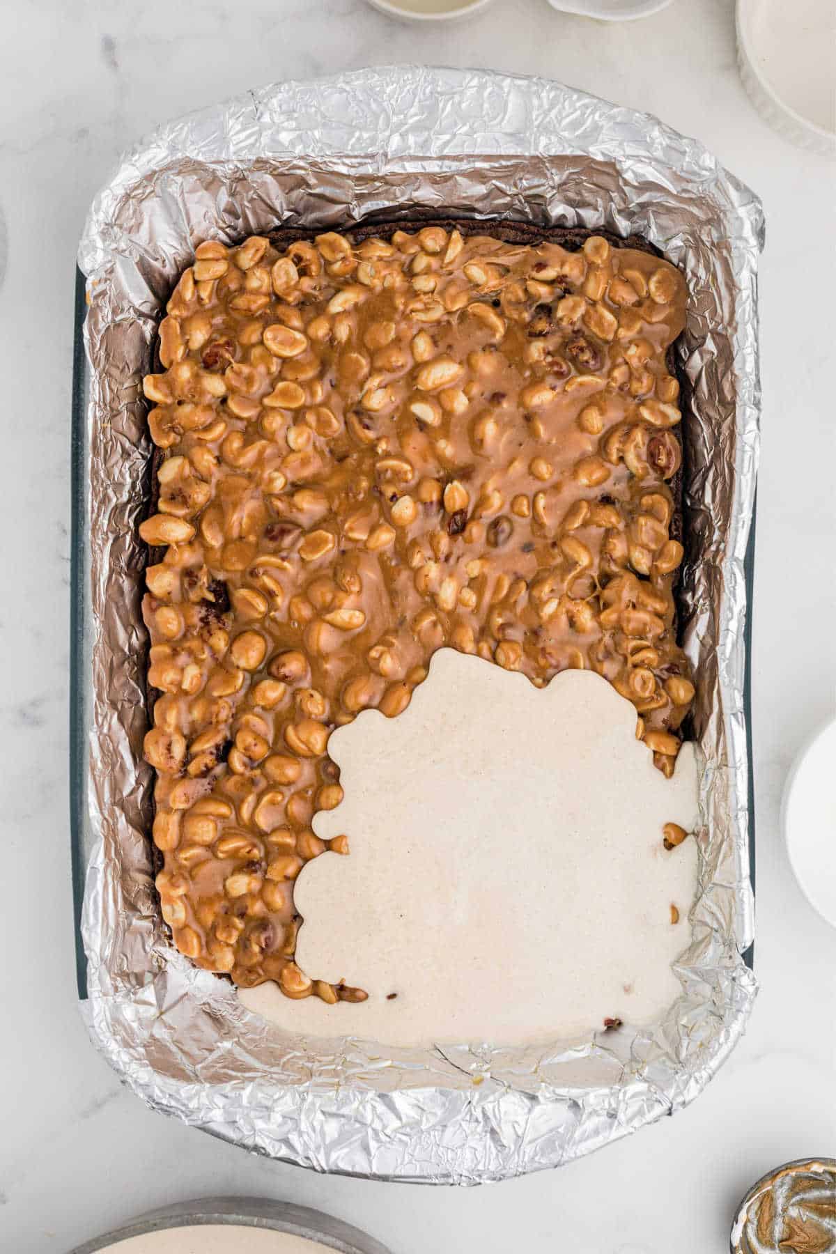 Nougat being poured over a nutty caramel layer in a baking dish.
