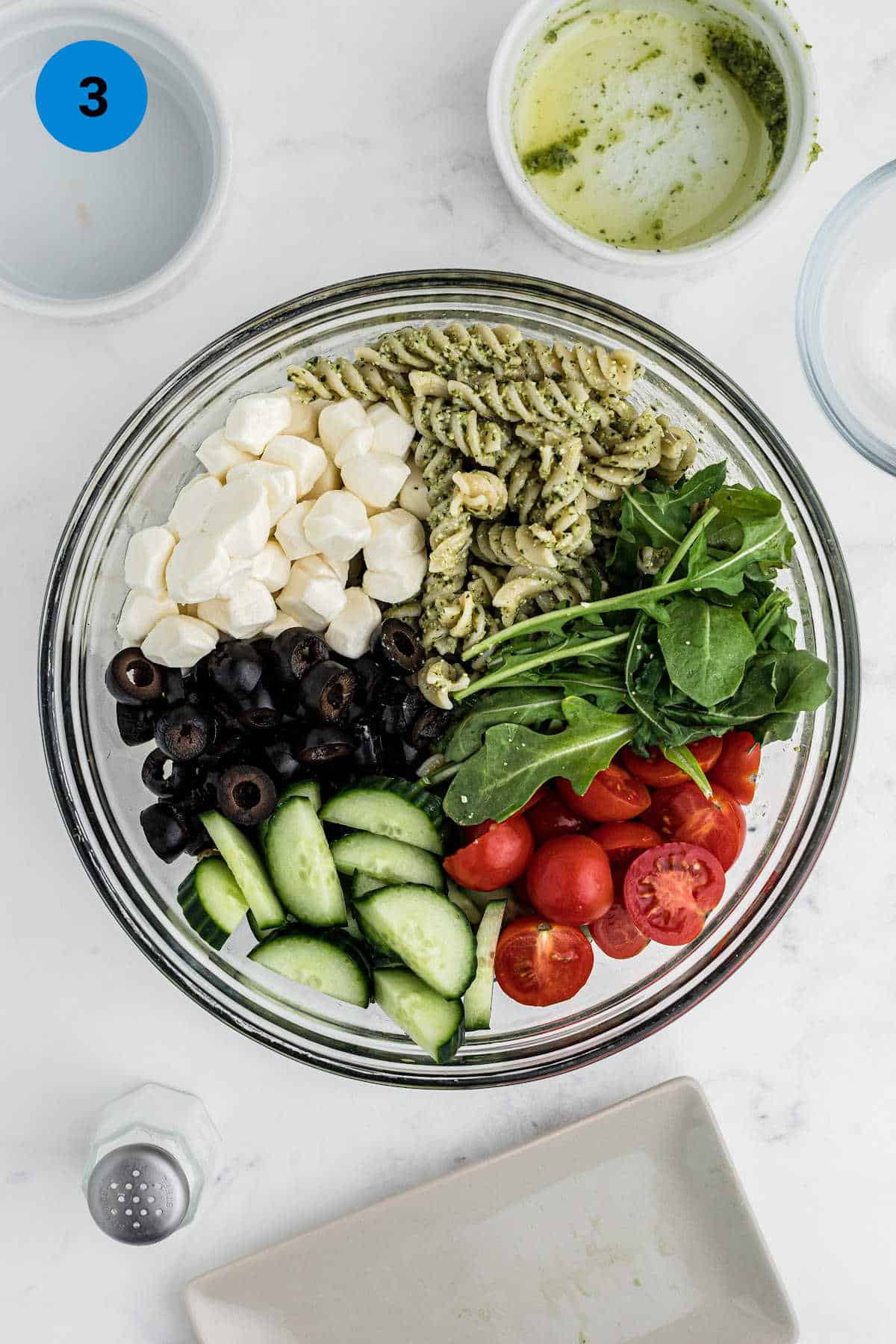Close up overhead shot of a bowl of ingredients to make a pesto pasta salad.