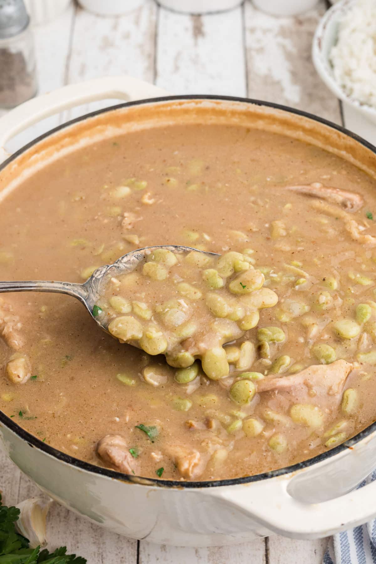 A spoon digging into a pot of chicken and lima beans.