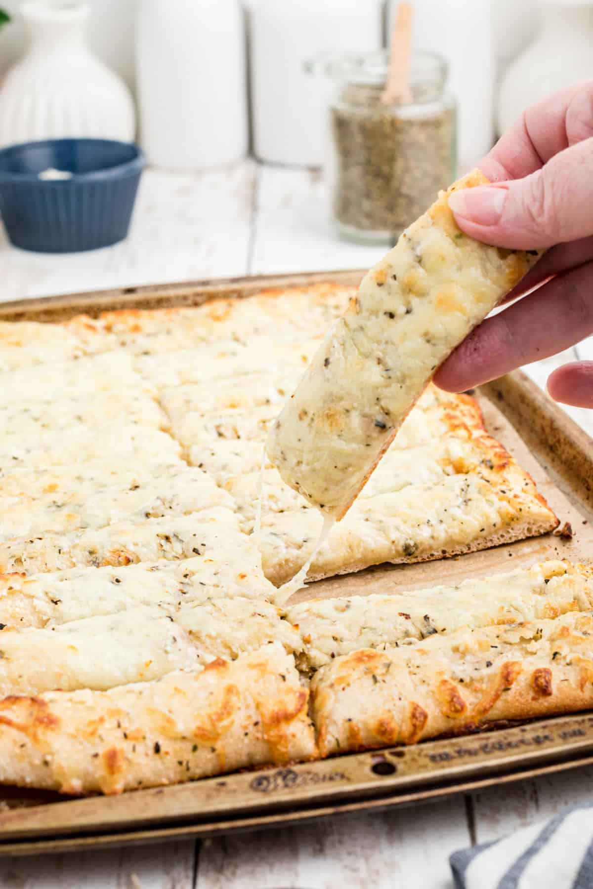 Someone lifting a piece of Italian Cheese Bread off of a baking sheet.