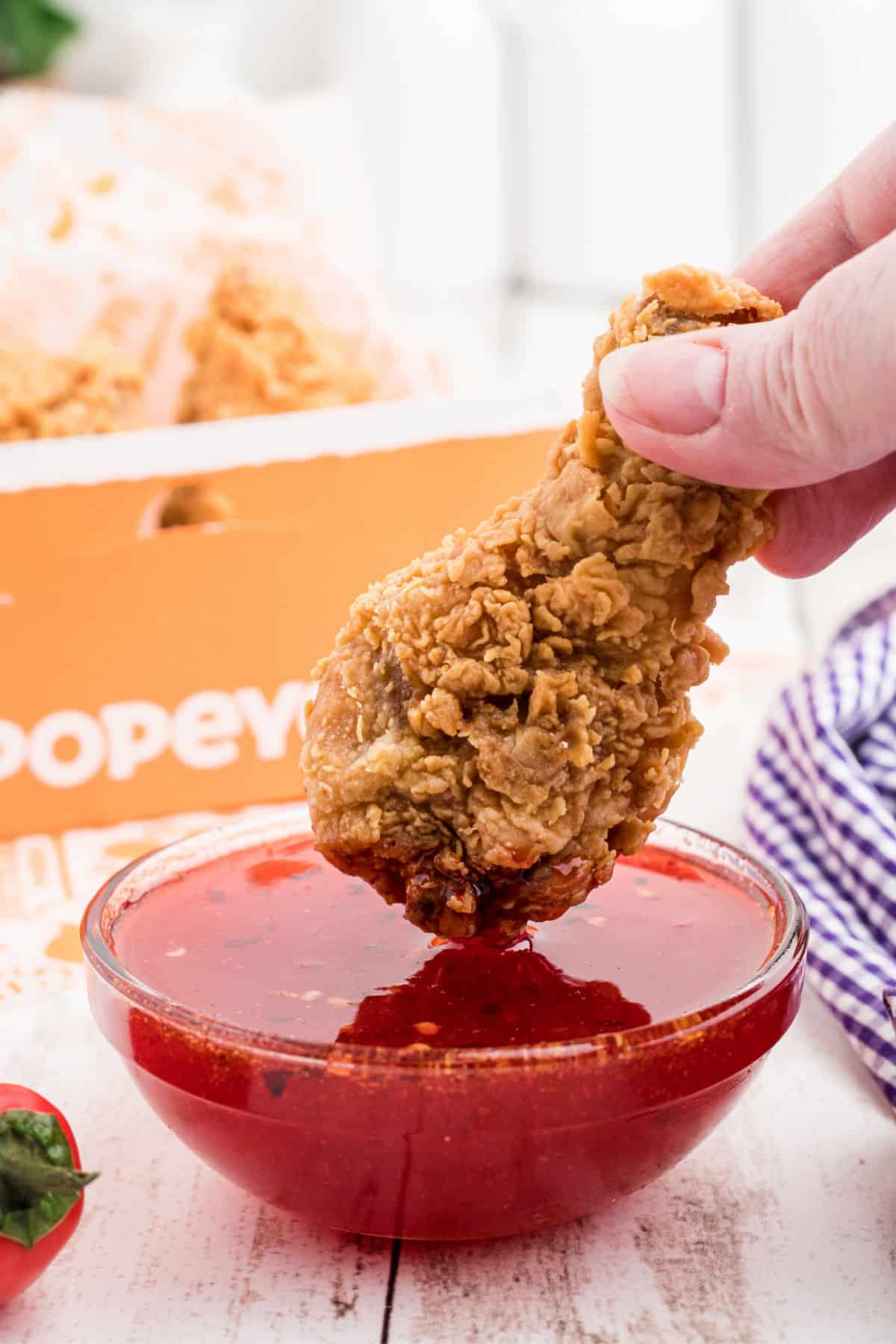 A popeyes chicken being dipped into homemade sweet heat sauce.