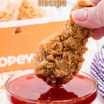 Piece of popeyes chicken being dipped into a homemade sweet heat sauce with text overlay for pinterest.