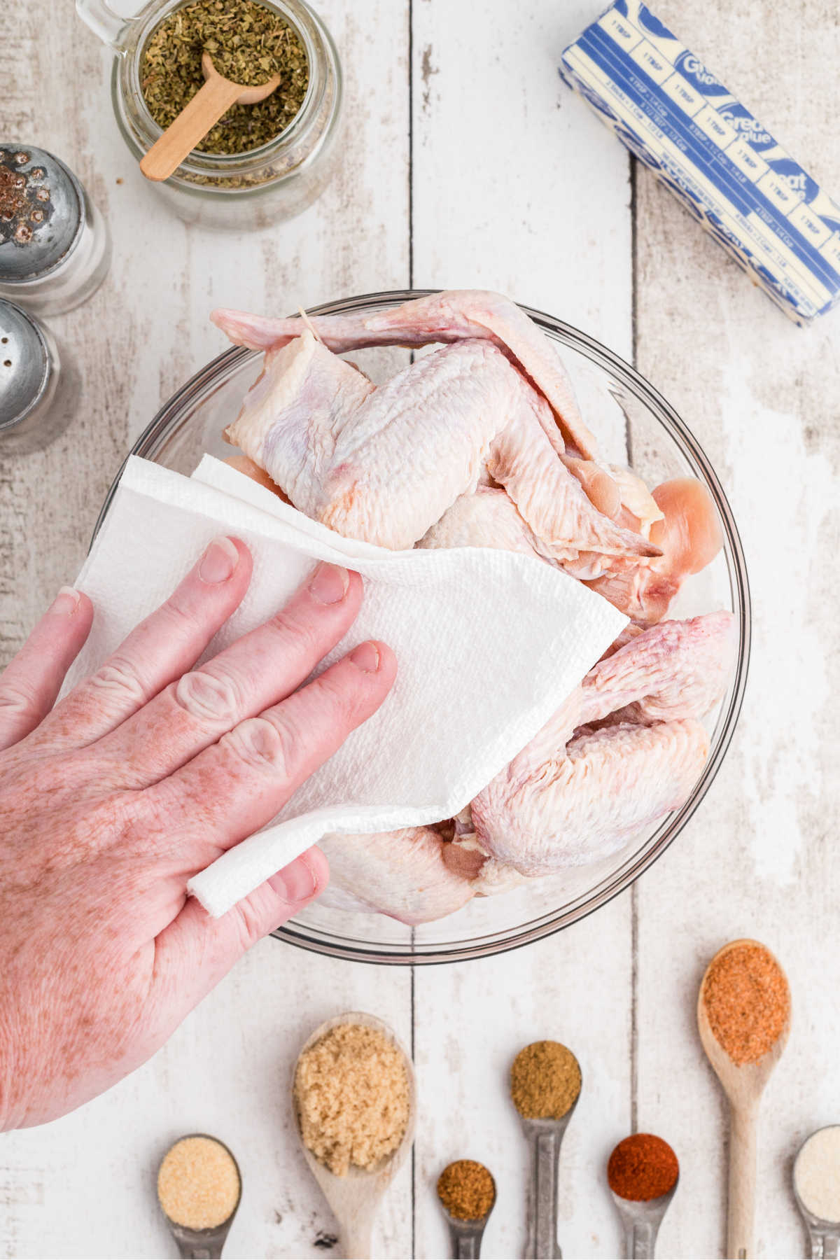 A bowl of chicken wings being patted dry with a paper towel.