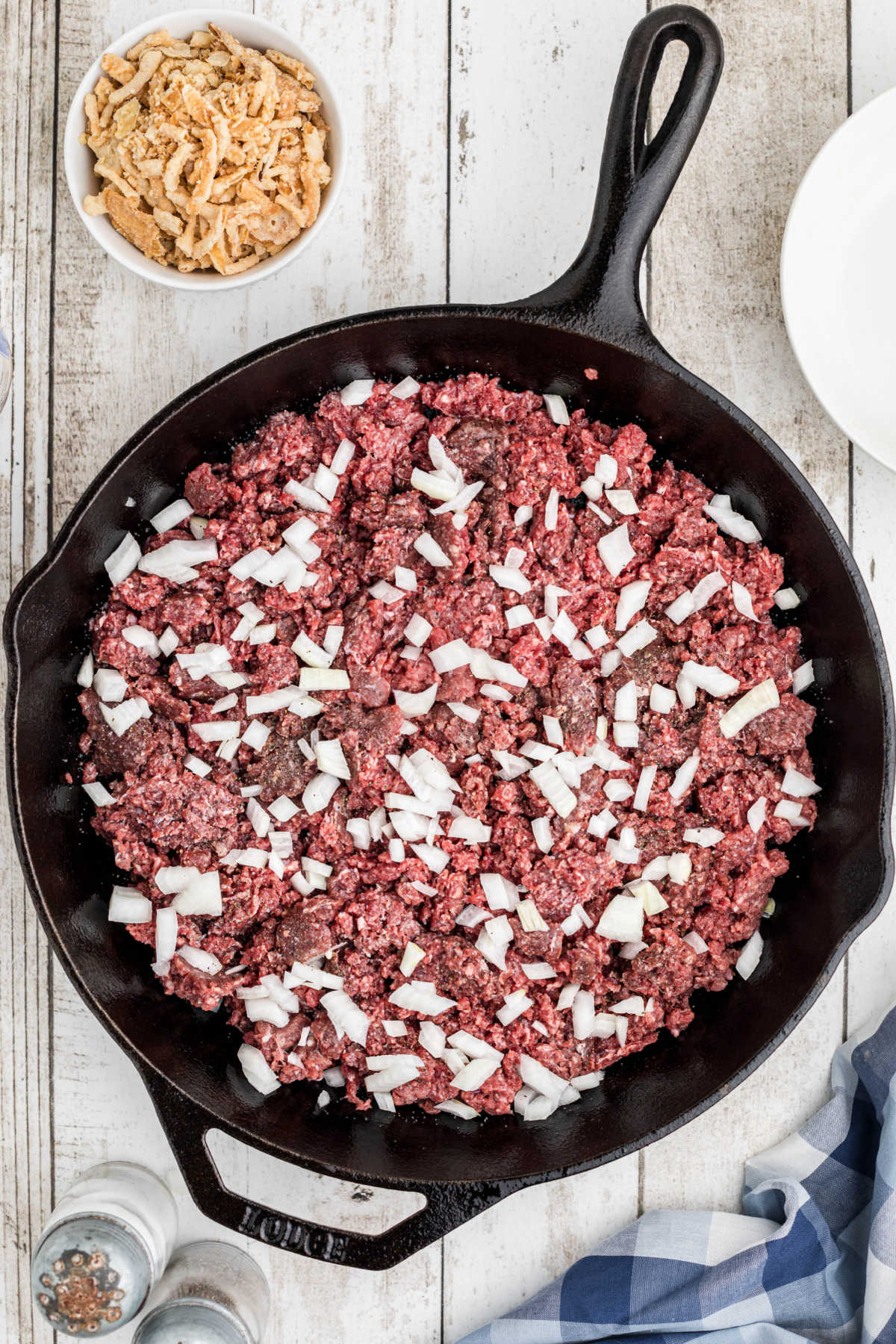 Overhead image of a cast iron skillet with ground beef topped with onions.