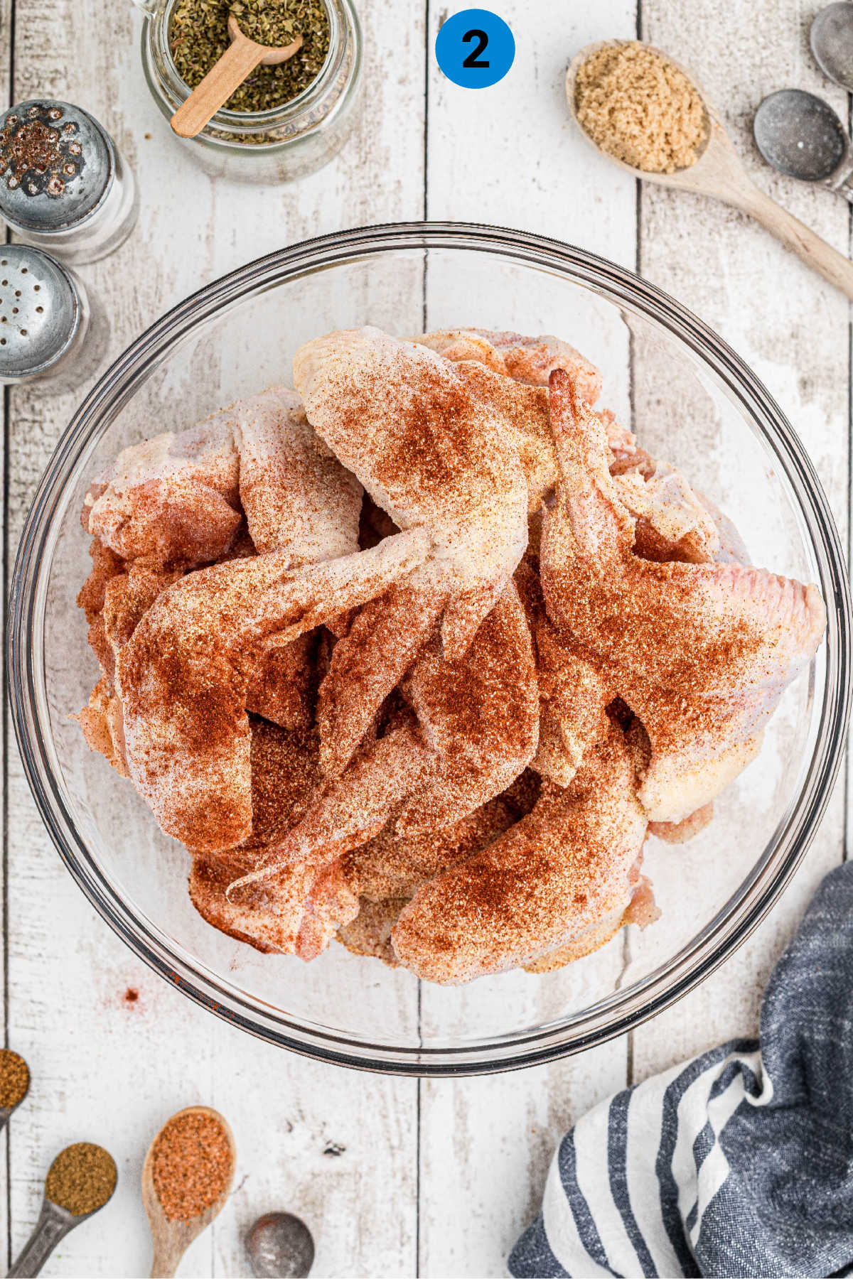 Chicken wings in a bowl with seasoning sprinkled on top.