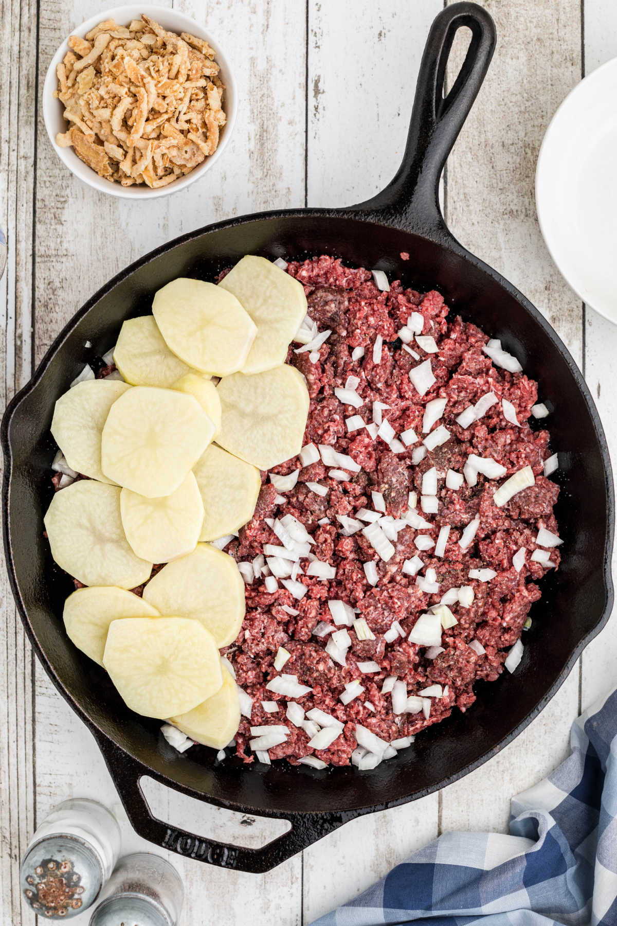 Overhead image of a cast iron skillet with a layer of ground beef, onions then sliced potatoes.