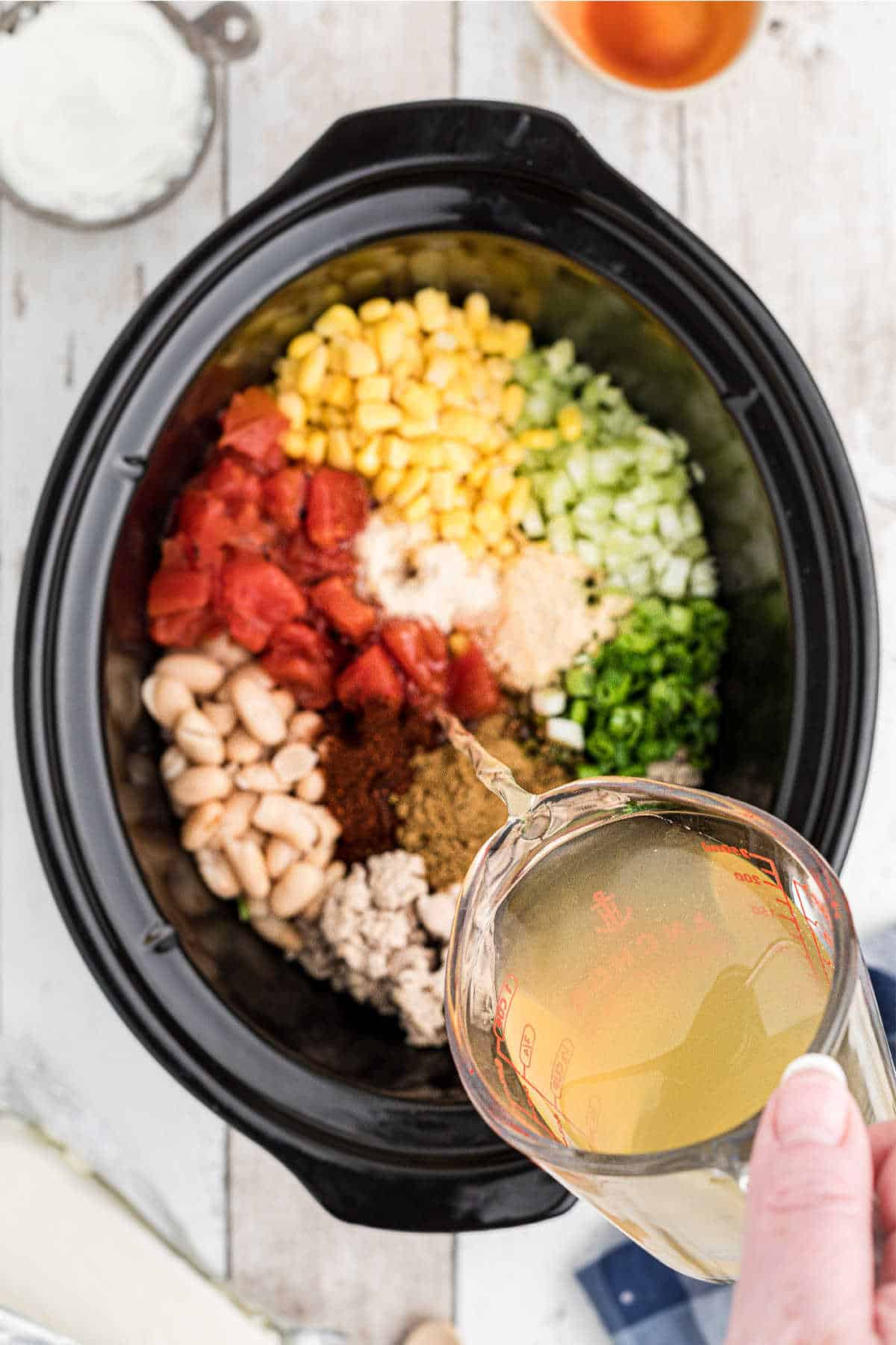 Chicken broth being poured into a crock pot full of ingredients.