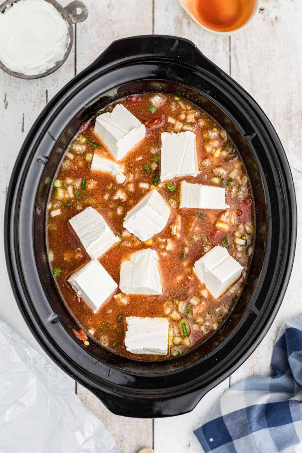 Chunks of cream cheese being added to a chili.