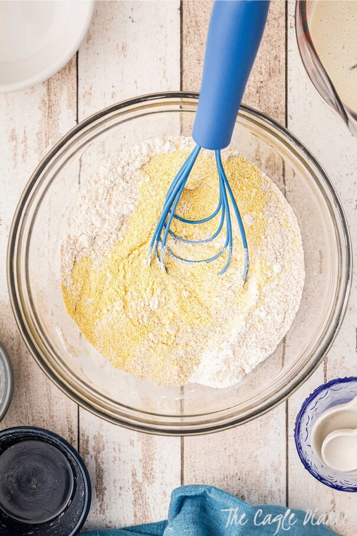 A bowl with some batter and dry flour with a blue whisk.