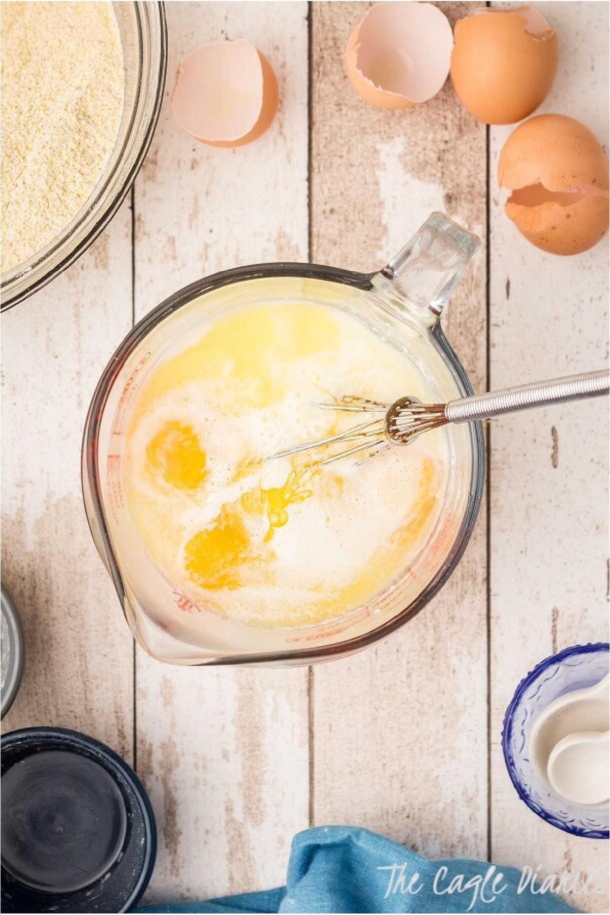 A glass measuring jug with eggs and milk being whisked.