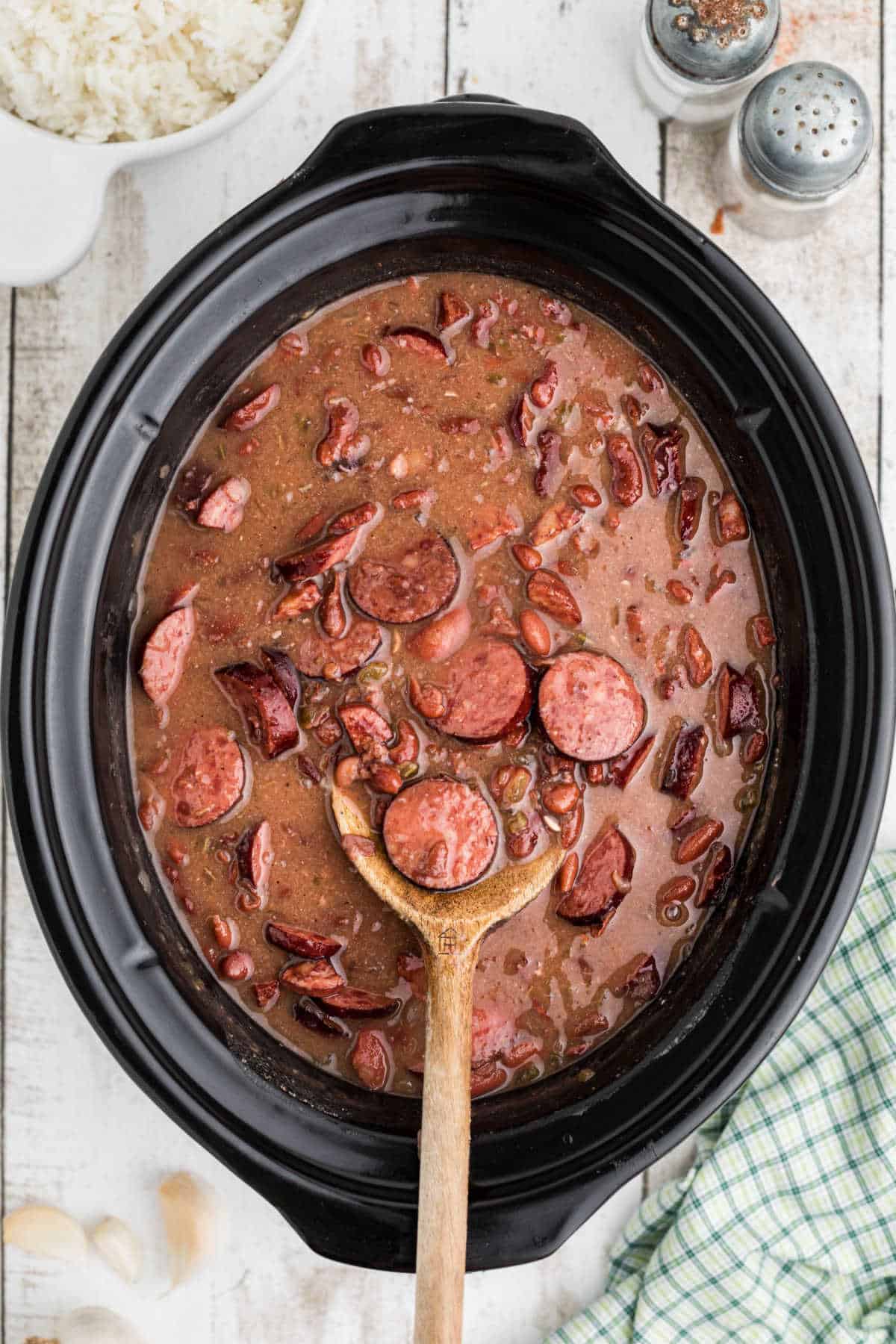 A spoon resting in a slow cooker with red beans and rice.