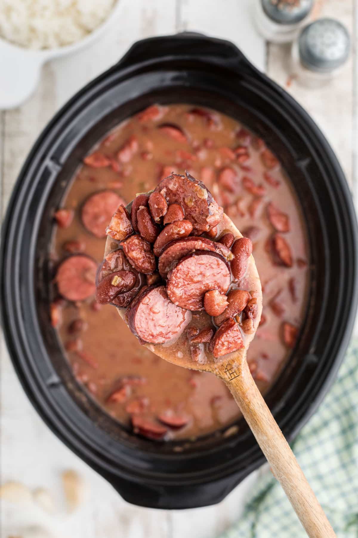 A spoon lifting some red beans out of a slow cooker.