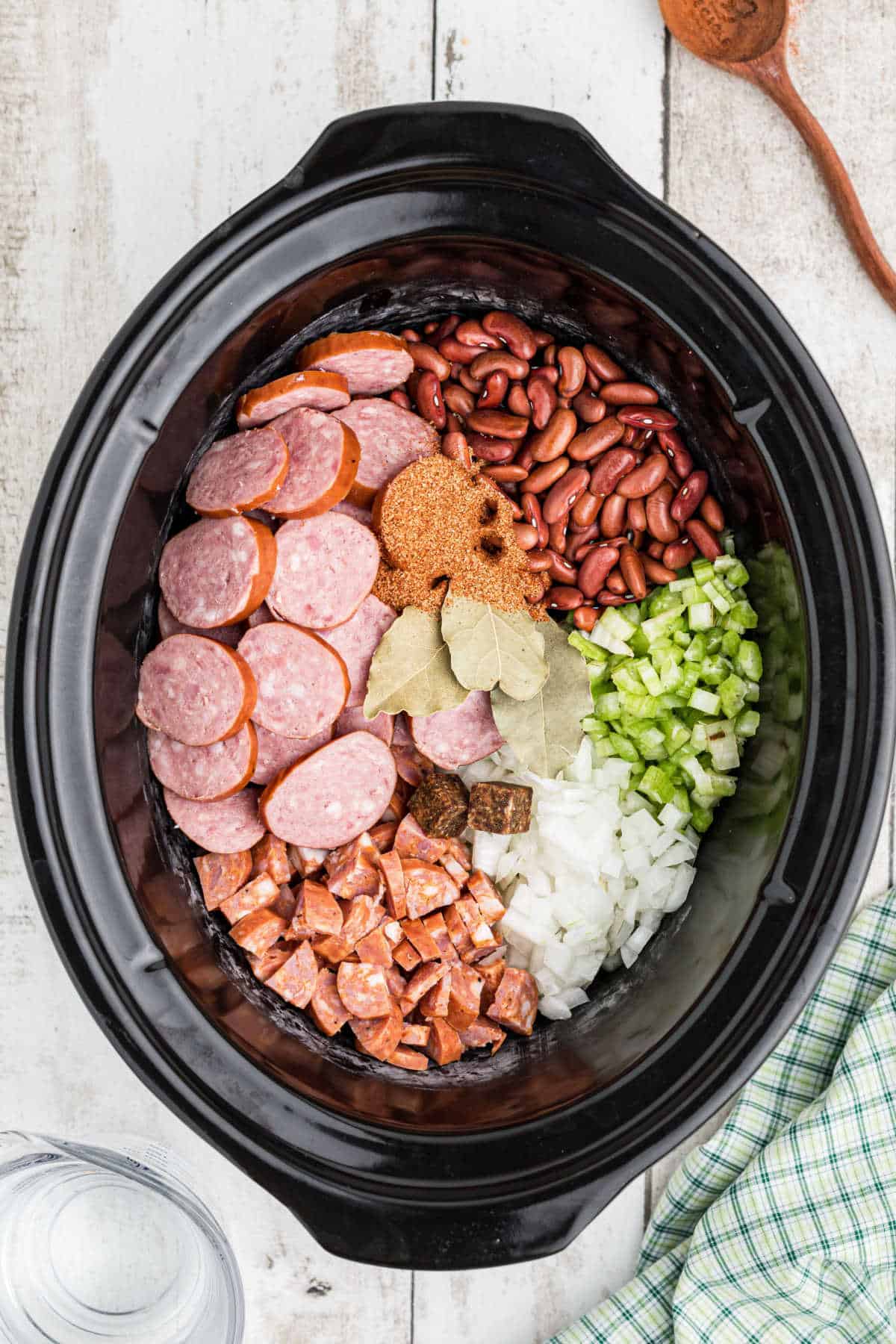 AN overhead image of a crock pot filled with ingredients needed to make a Cajun red beans and rice recipe.