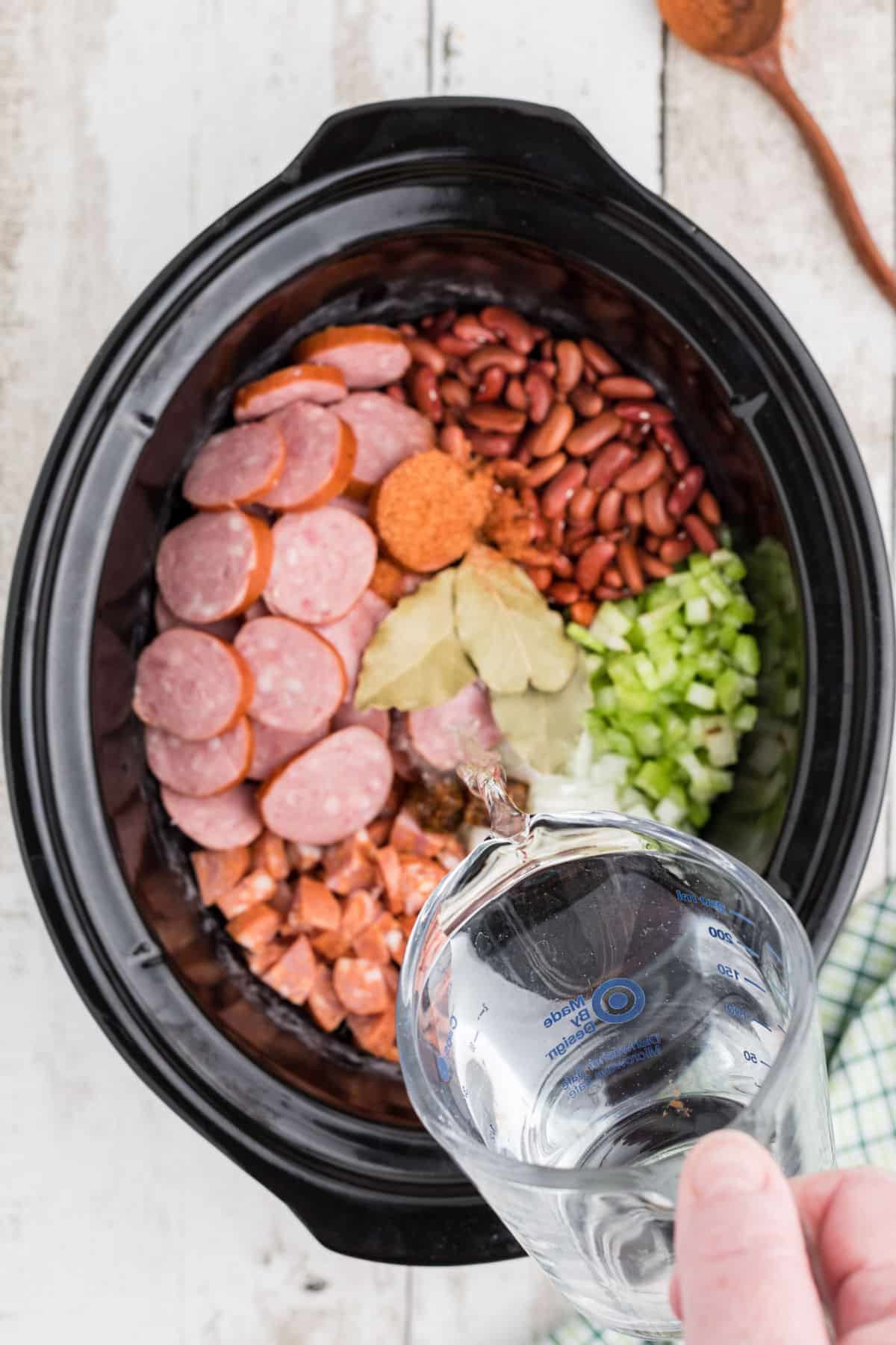A slow cooker cajun red beans and rice recipe with water being poured in.
