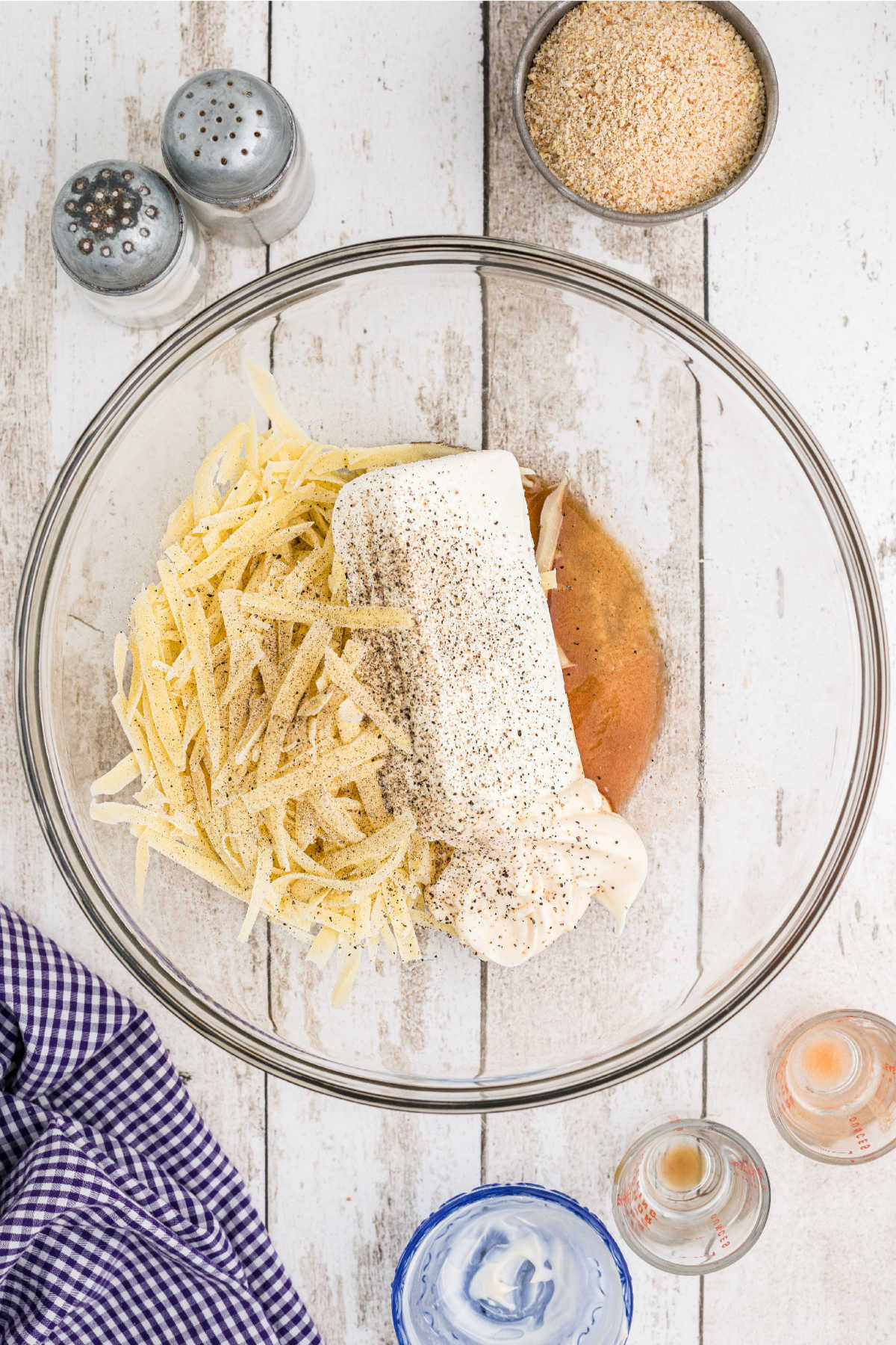 A mixing bowl with grated cheese, cream cheese and seasoning.
