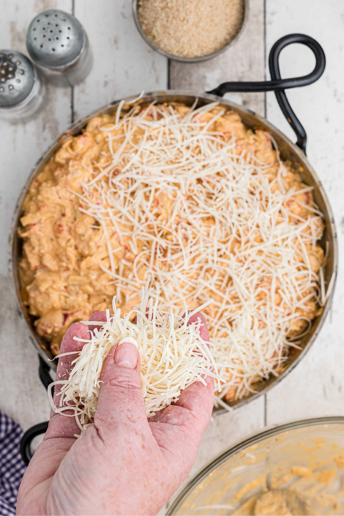 A cheesy crawfish mixture in a skillet being topped with cheese.