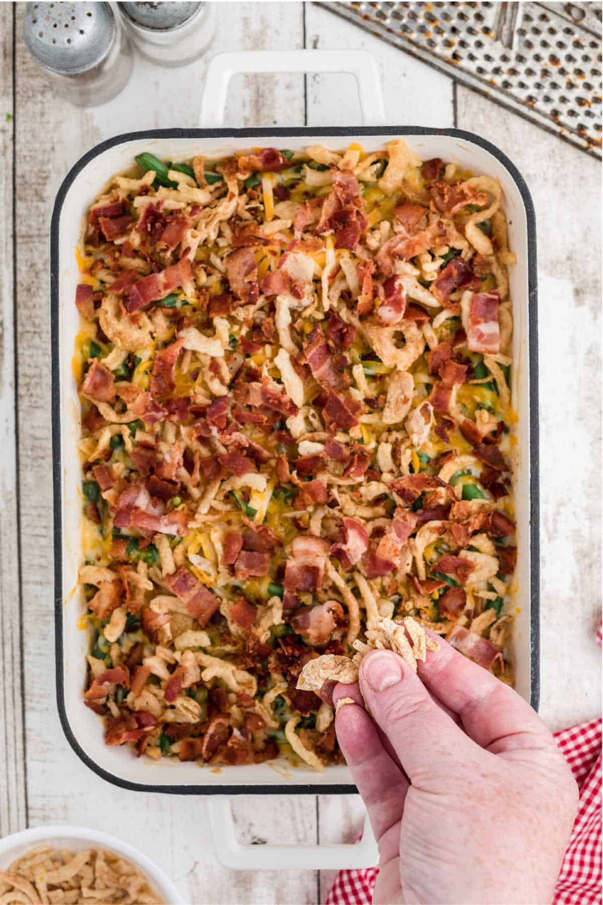 Fried onions being sprinkled on top of a green bean casserole.