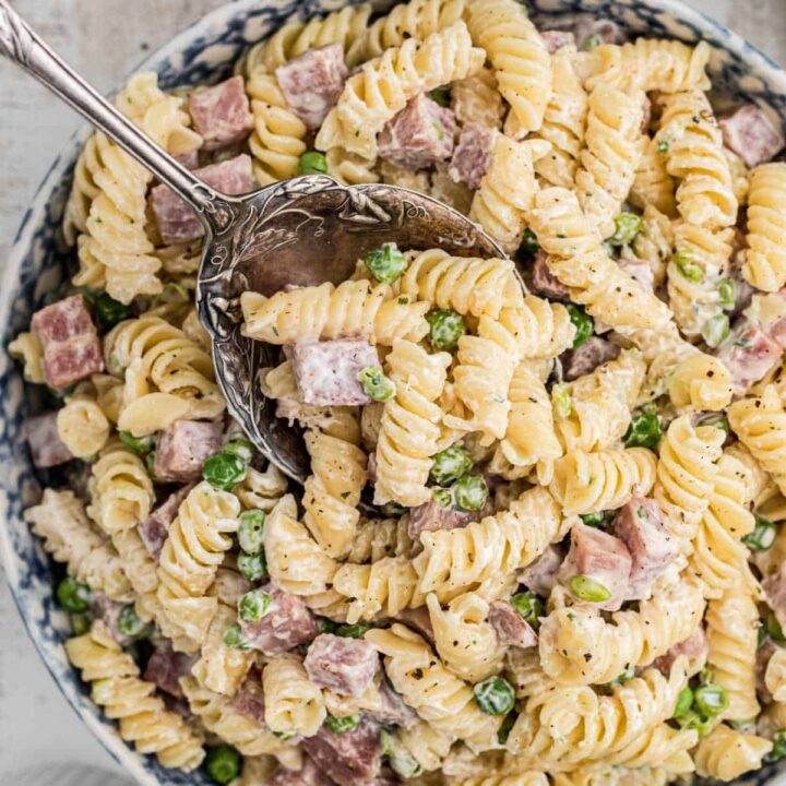 Close up of a bowl of Ruby Tuesday ham and pea pasta salad with a spoon digging in.