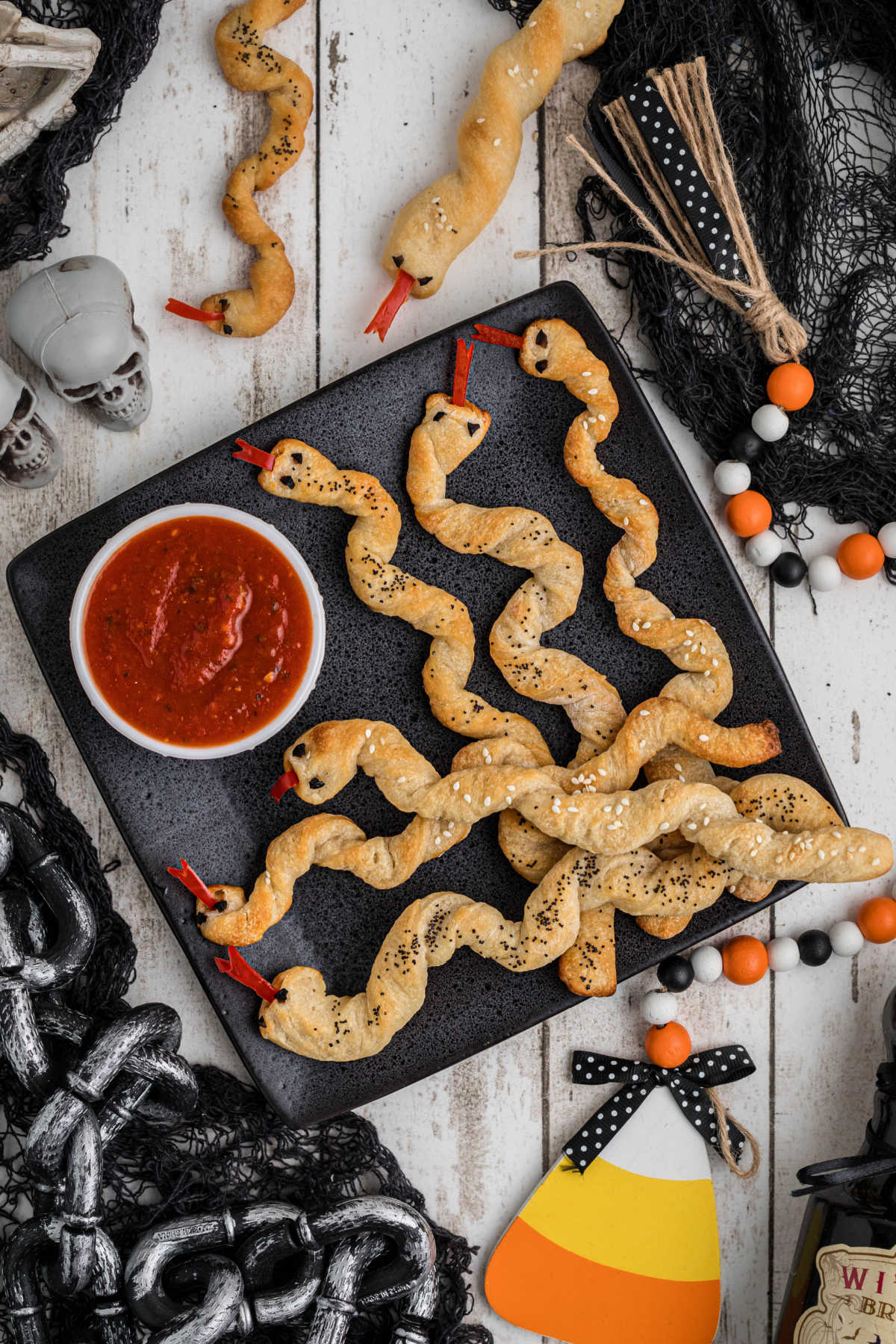 Breadstick rattlers on a plate with Halloween decorations all around.