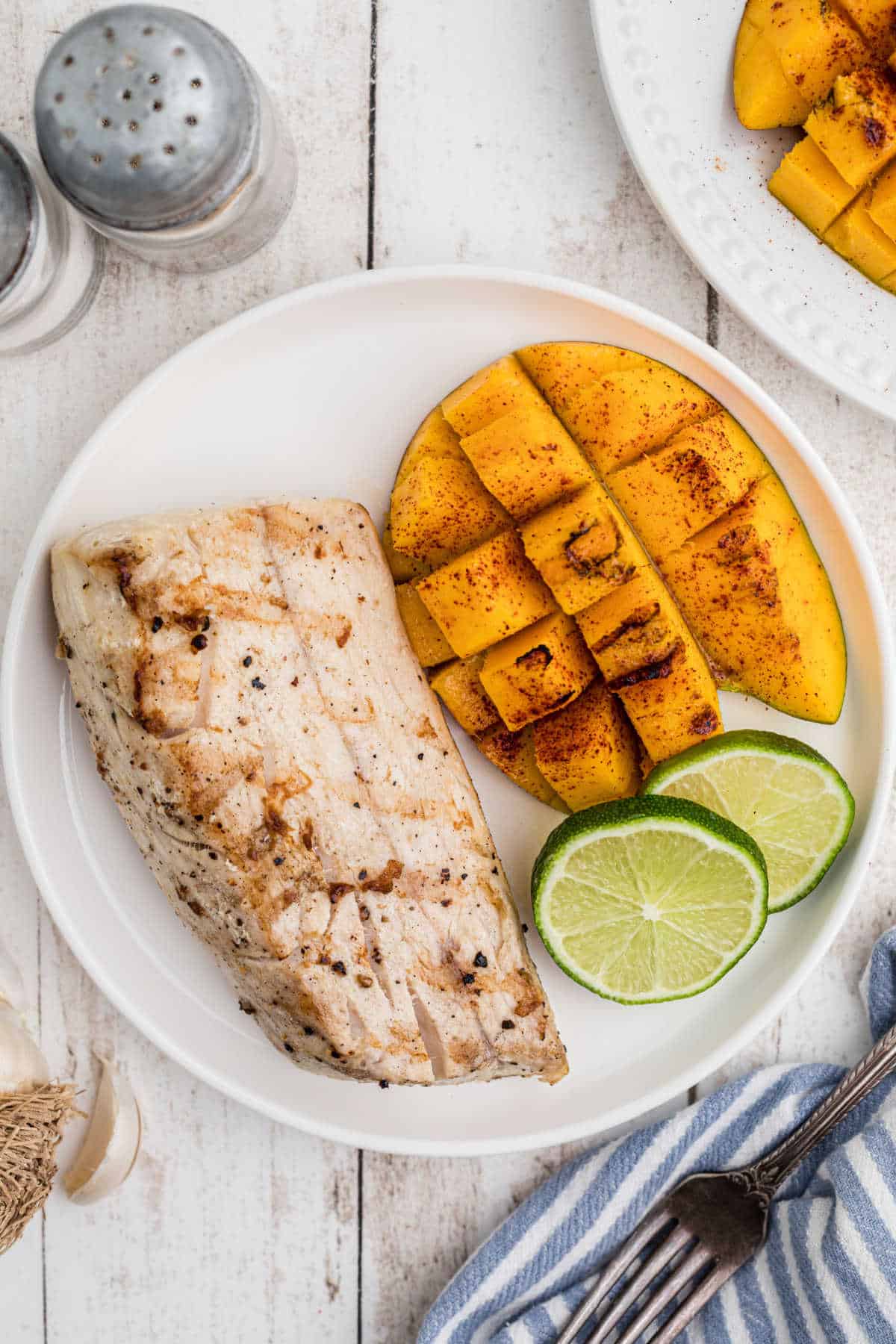 Overhead view of a plate with grilled cobia and mango with lime slices.