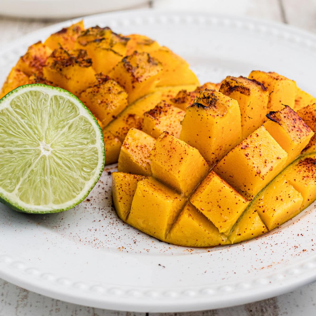 A close up of a plate with two pieces of grilled mango and a lime.