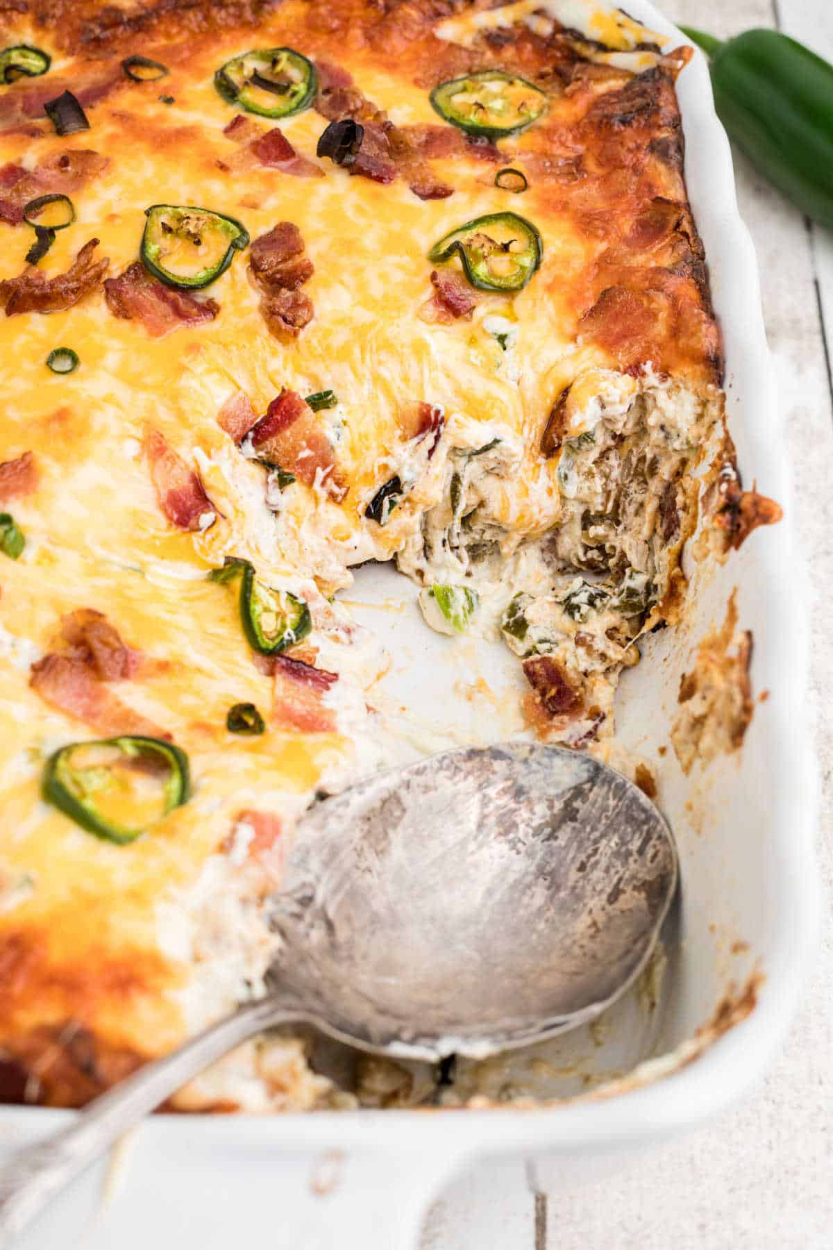 A Jalapeno Popper Tater Tot Casserole with some scooped out and a spoon left there.