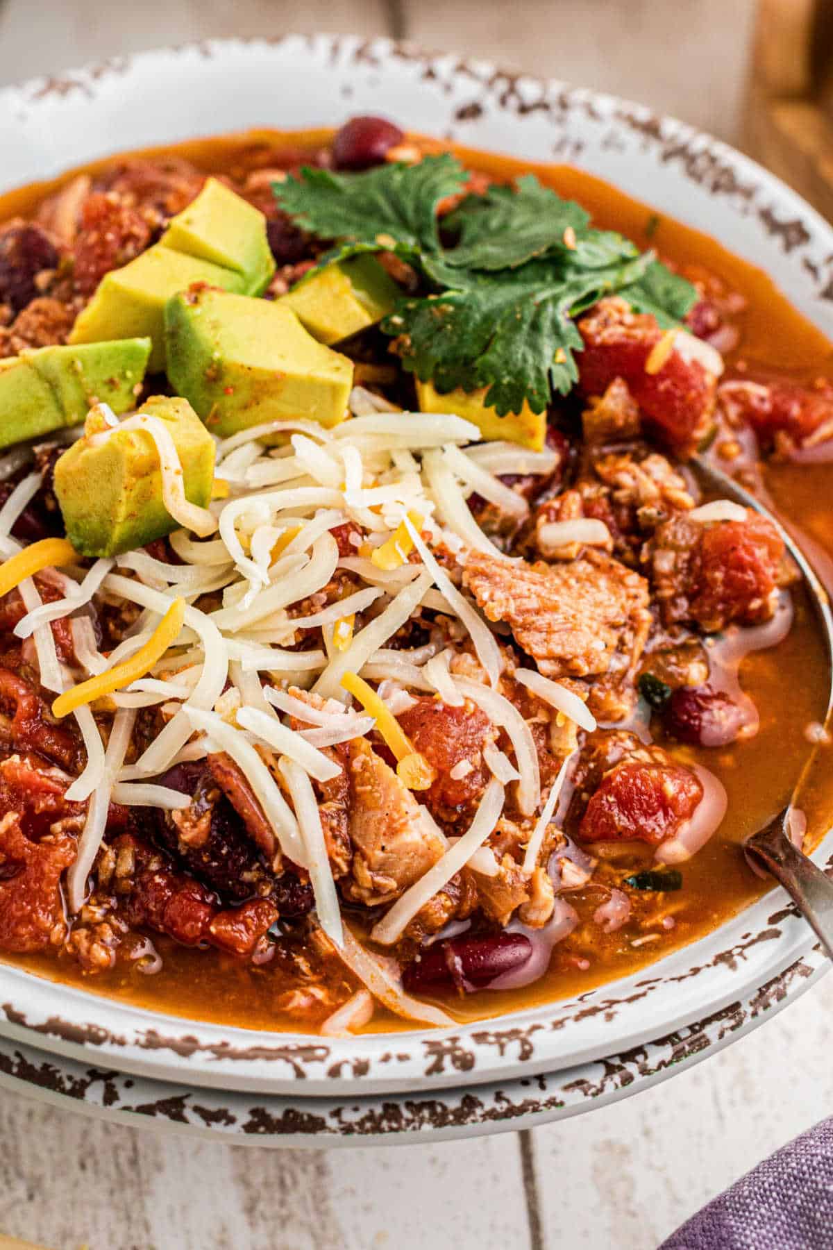 Close up of a bowl of Dutch oven turkey chili with cheese and avocado sprinkled on top.