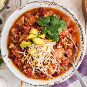 Overhead shot of a bowl of Dutch Oven turkey chili with cheese and avocado on top, cropped square.