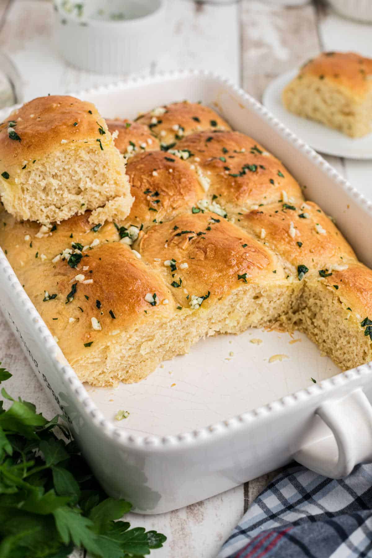 Garlic butter rolls in a baking dish with one standing on top.