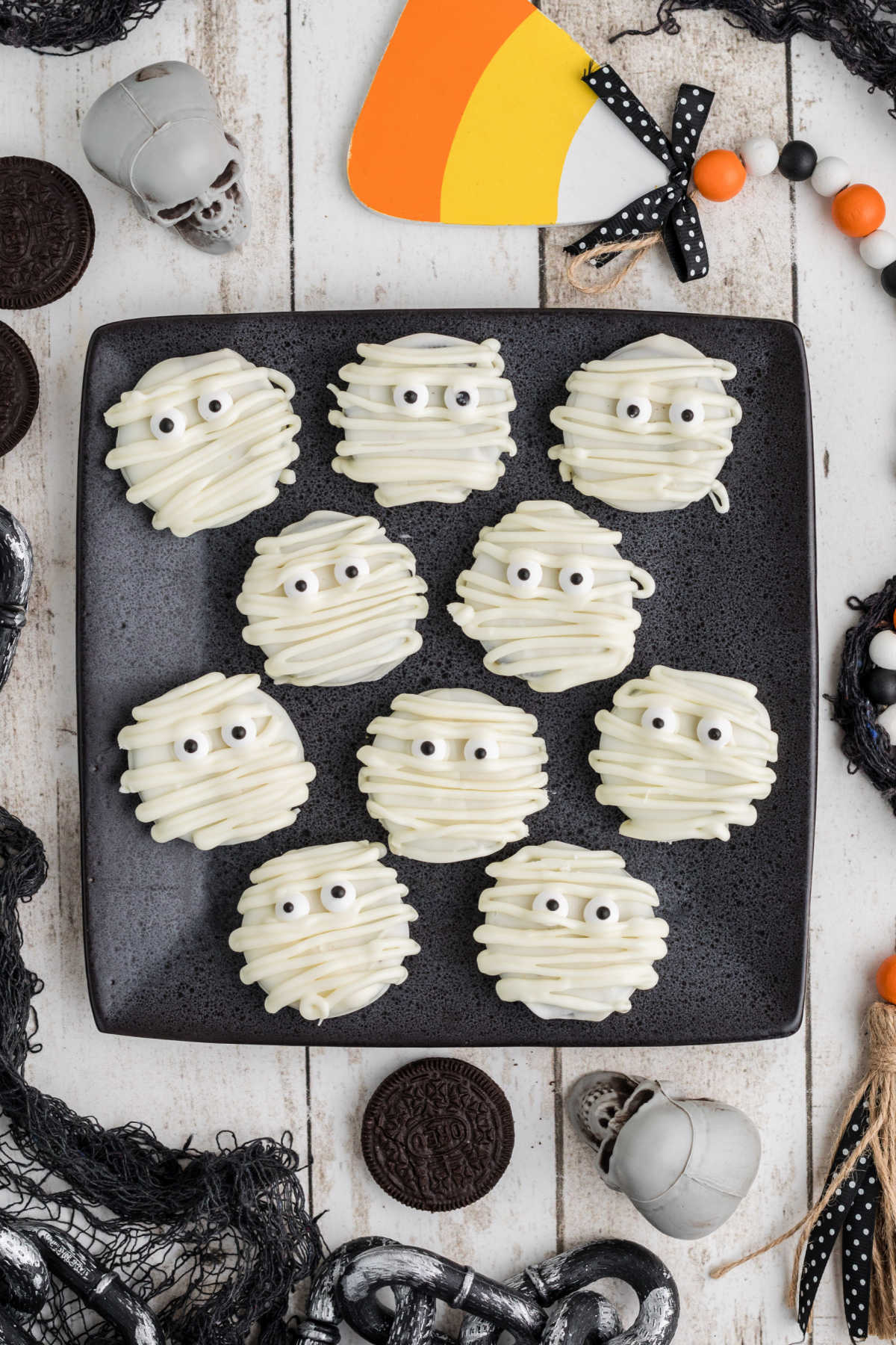 Mummy Oreos on a square black plate from overhead, with halloween decorations all around.