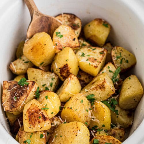Slow cooker roast potatoes recipe with a wooden spoon digging in.
