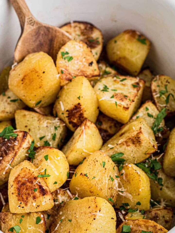 Slow cooker roast potatoes recipe with a wooden spoon digging in.