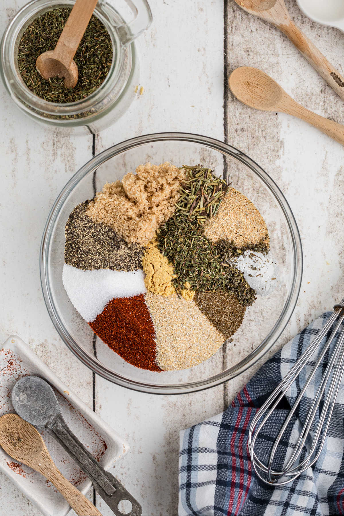 A glass bowl with a lot of different spices about to be mixed together.
