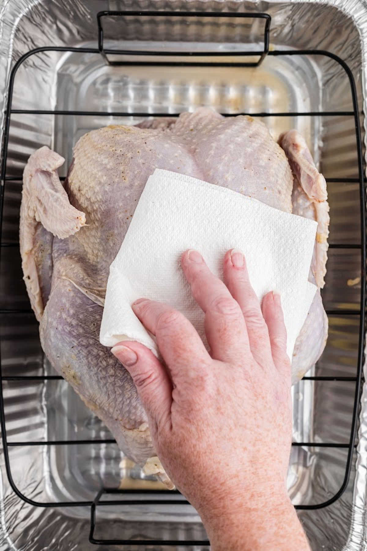 A hand patting a turkey dry with a paper towel.