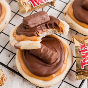 An image of two cookies, with a bite taken out of one - copycat crumbl twix cookies.