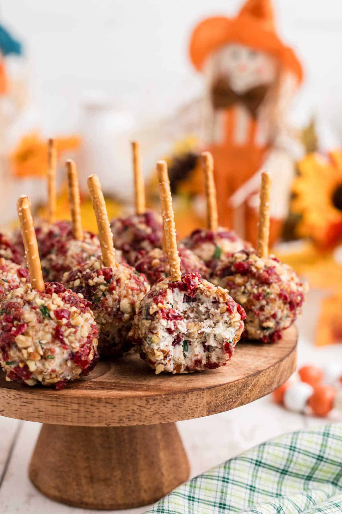 A close up of a cake stand that has cranberry pecan cheese ball bites, with pretzel sticks.