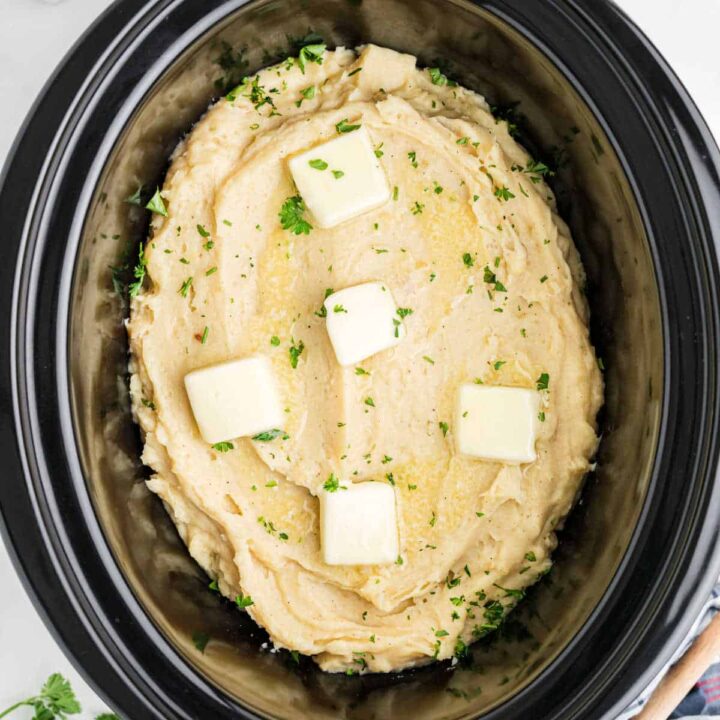 Overhead image of slow cooker mashed potatoes made with chicken broth, and pats of butter on top.