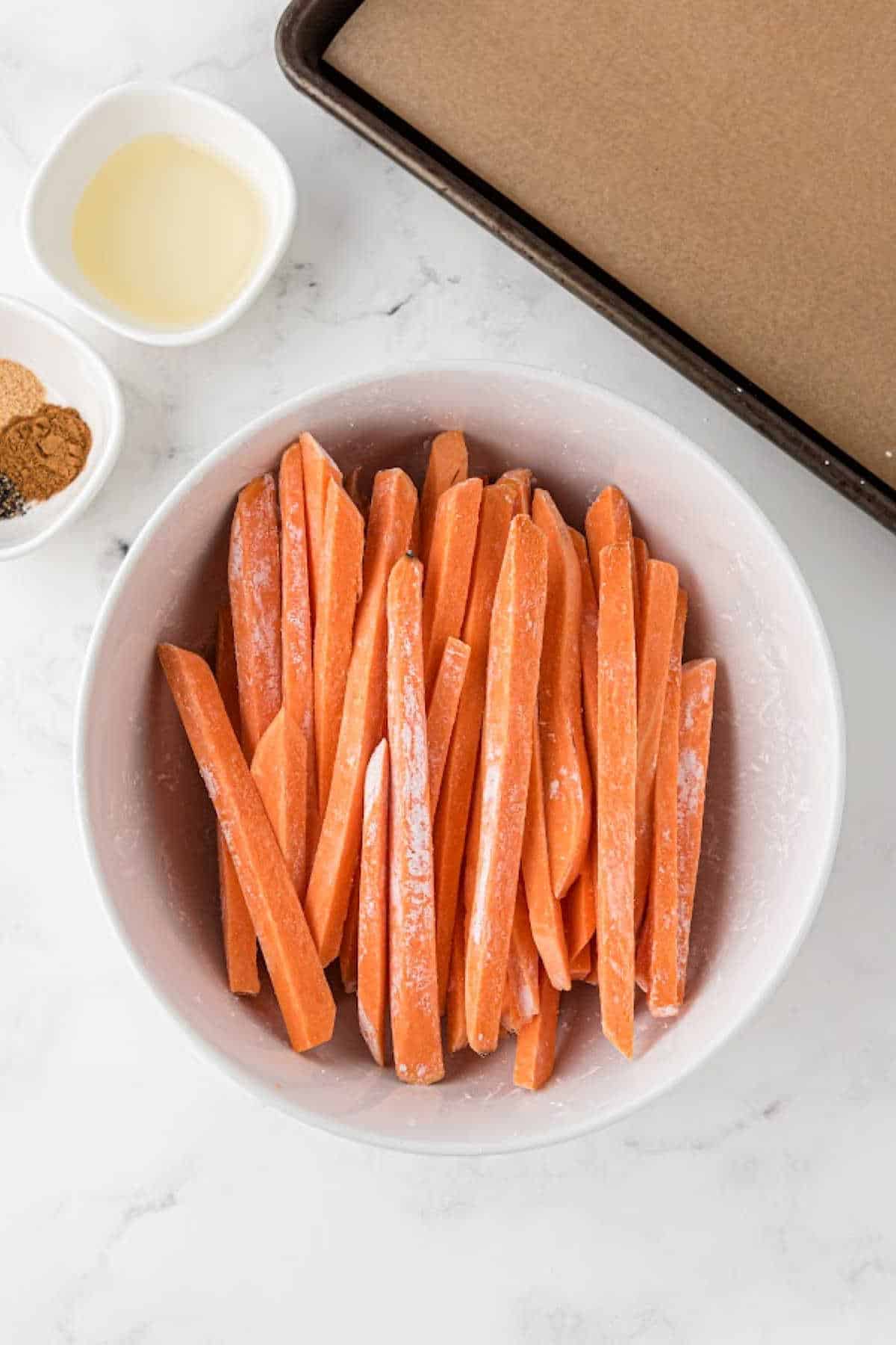 Sticks of sweet potato sticks in a bowl, with oil and ready to be coated with cornflour.