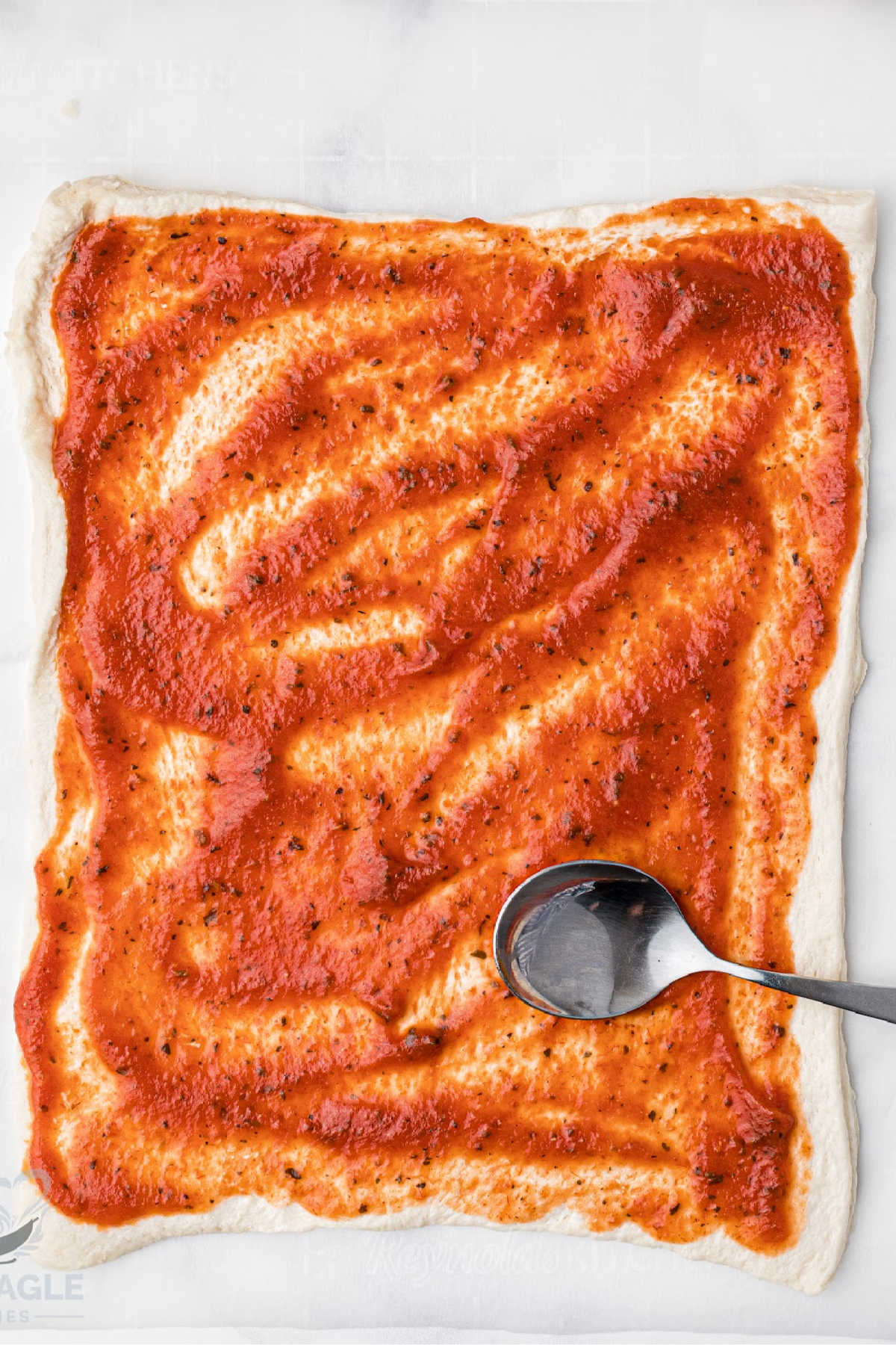 Pizza sauce spread on puff pastry sheet.