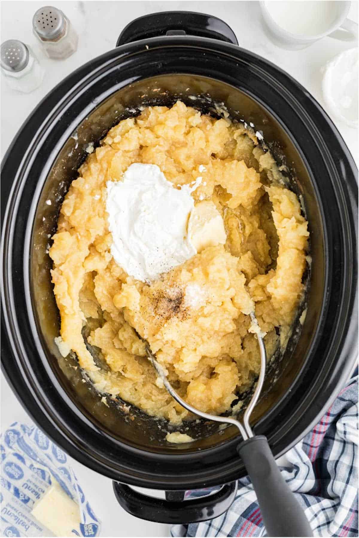Sour cream and butter added to a slow cooker full of mashed potatoes.