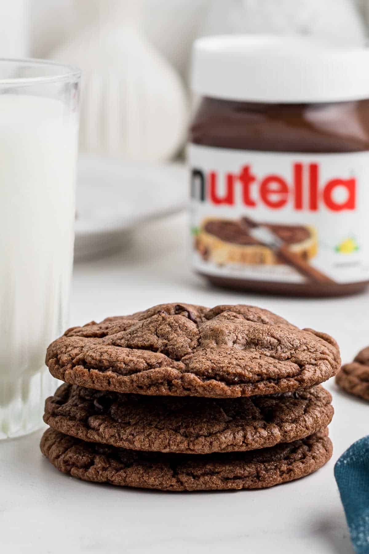 3 Nutella brownie cookies in a stack, with a jar of Nutella in the back.