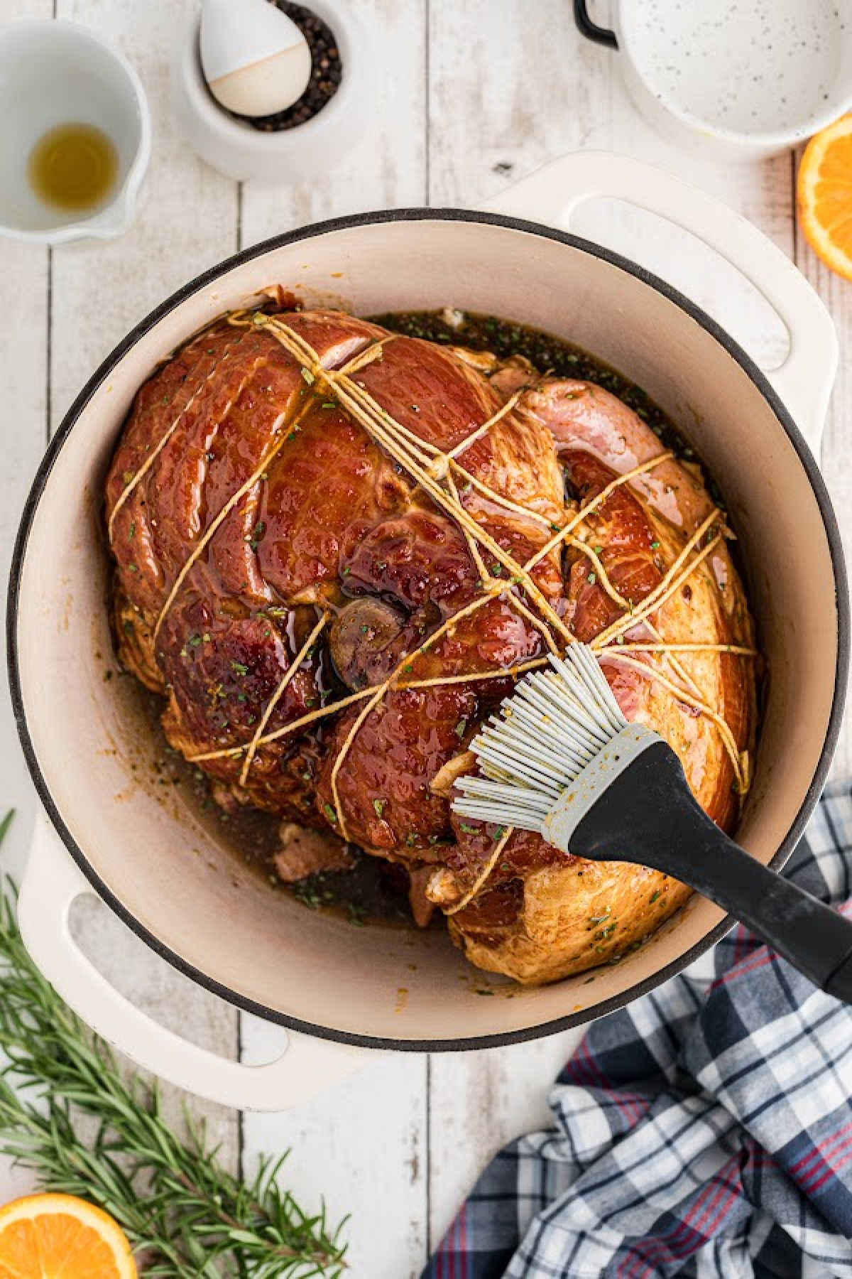 A trussed ham, being brushed with a glaze inside a Dutch oven.
